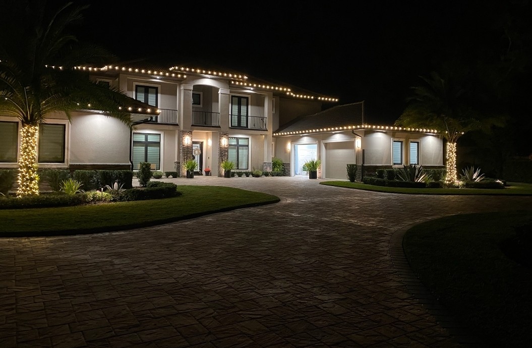 Two-story home lit with warm white C9 roofline lights on both levels and two wrapped palms
